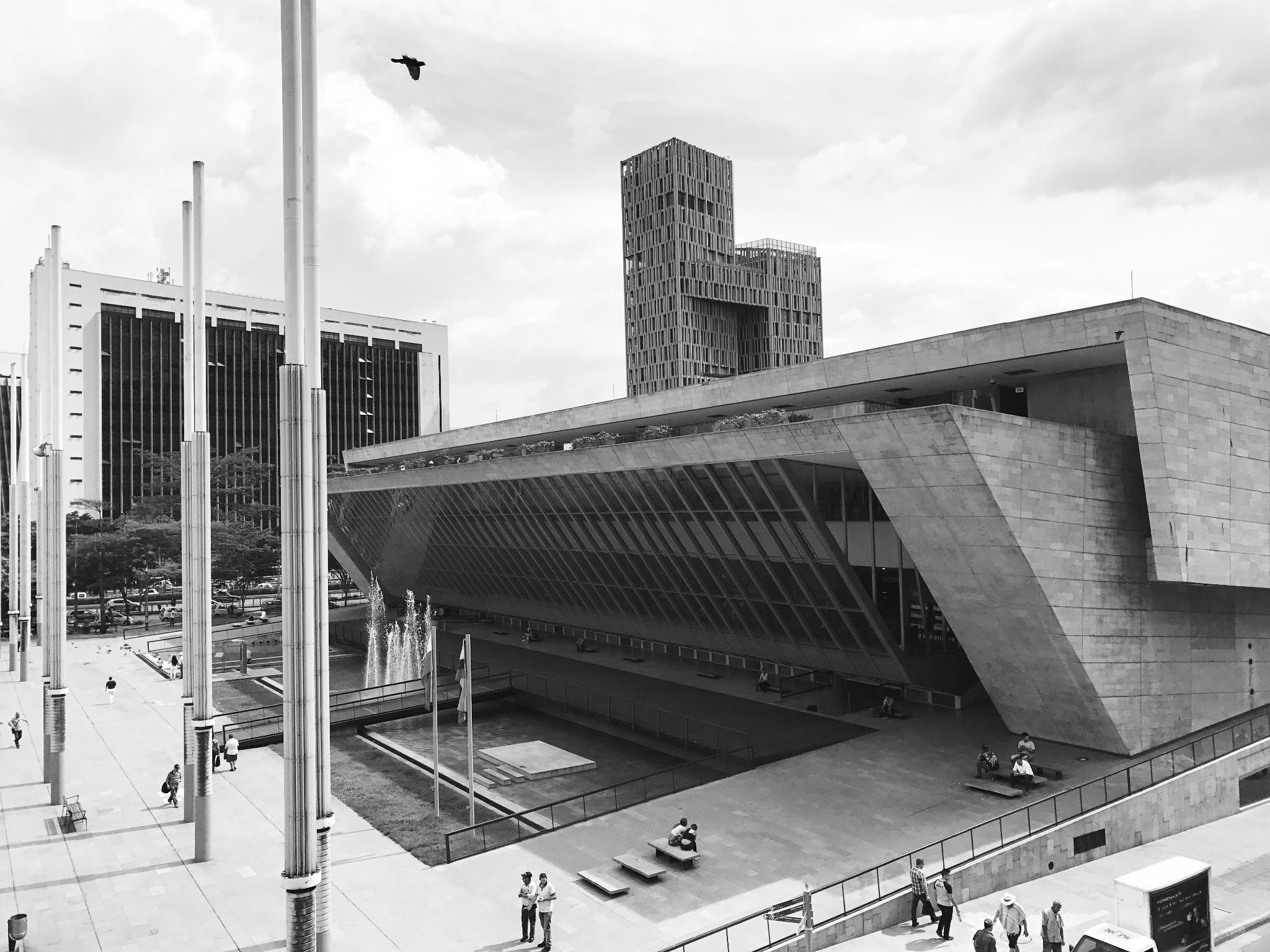 Keilförmiges Betongebäude an einem Platz, dahinter Hochhäuser