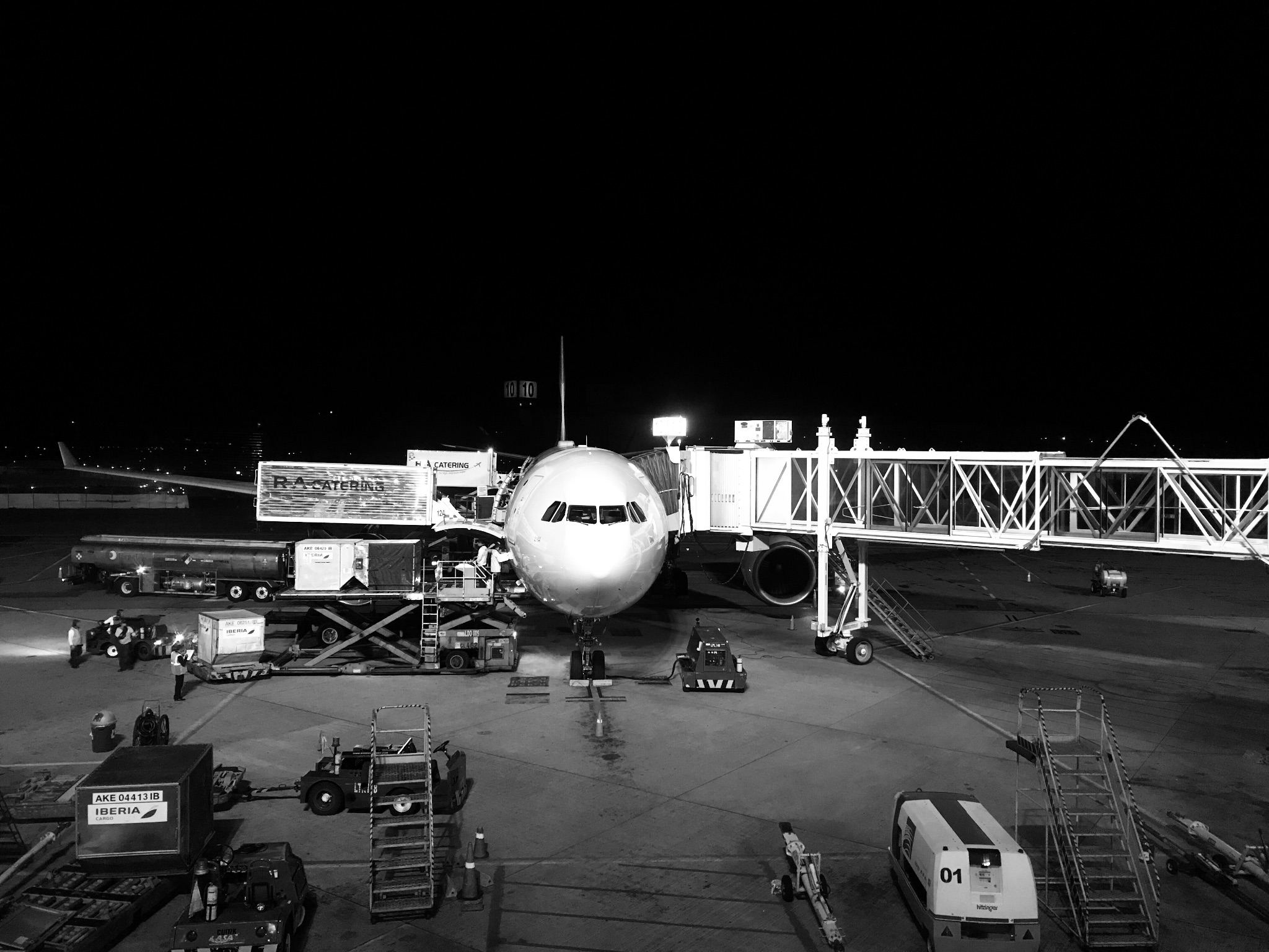 Flugzeug am Gate bei Nacht, umgeben von Vorfeldfahrzeugen
